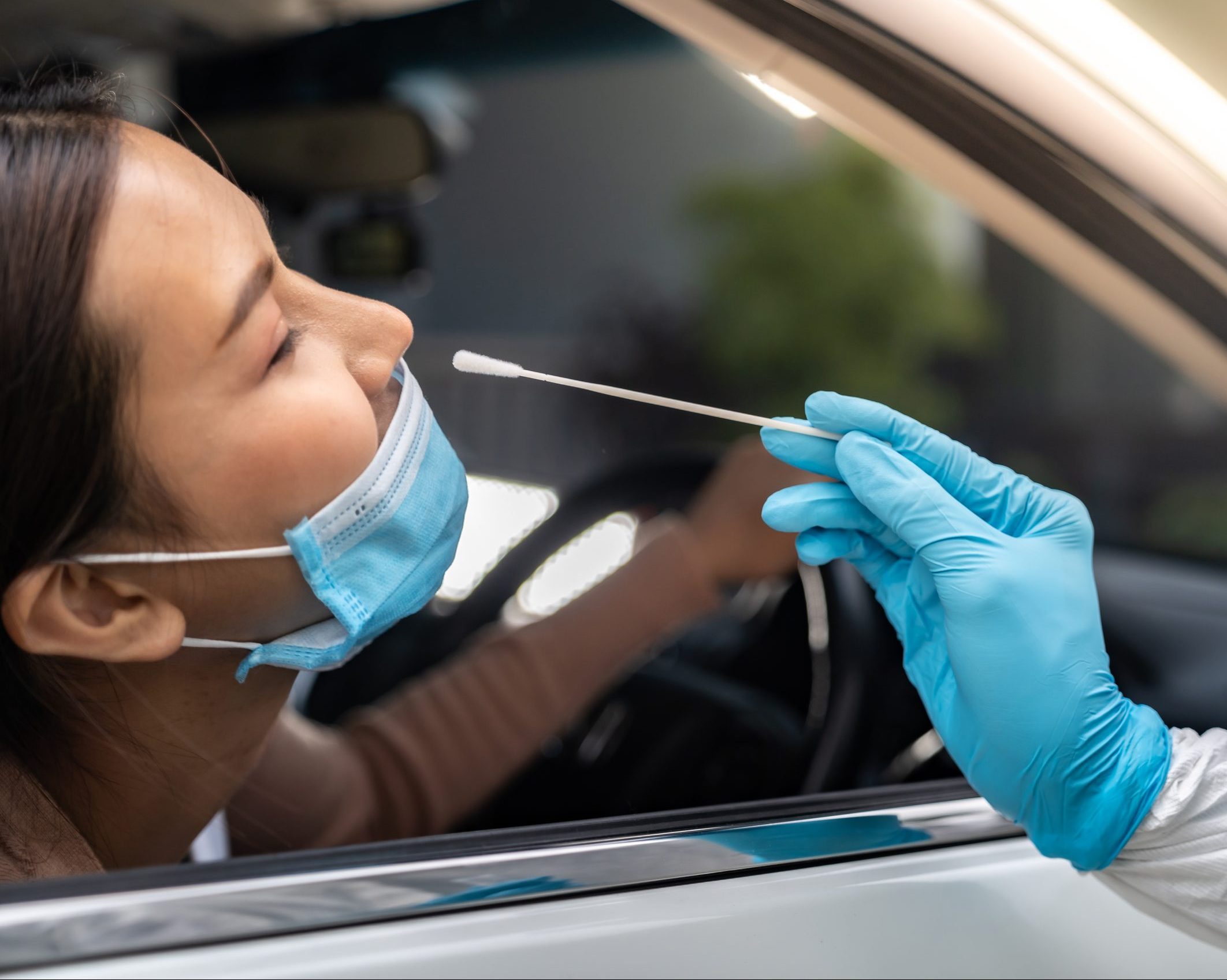 Portrait of asian woman drive thru coronavirus covid-19 test by medical staff with PPE suit by nose swab.